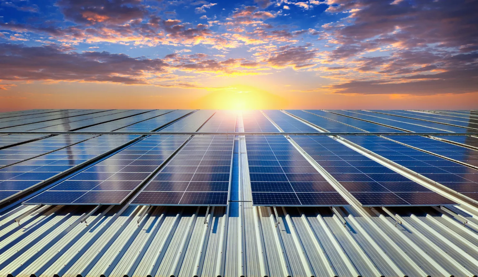 Rows of solar modules mounted on a corrugated metal roof, photographed into a low sun at the end of the day
